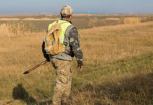 Caccia in Abruzzo, presentata nuova proposta di calendario venatorio caccia in Abruzzo: cacciatore di spalle per i campi, indosso il giubbotto alta visibilità, fucile nella mano sinistra