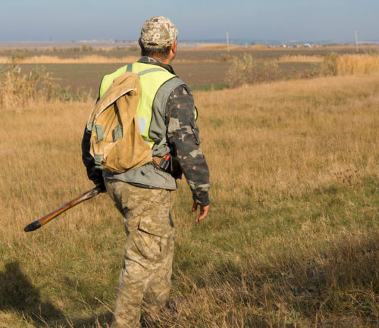 Caccia in Abruzzo, presentata nuova proposta di calendario venatorio caccia in Abruzzo: cacciatore di spalle per i campi, indosso il giubbotto alta visibilità, fucile nella mano sinistra