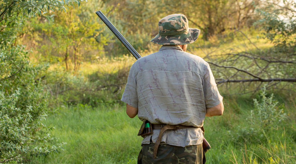 caccia in puglia: cacciatore di spalle con cappello mimetico e fucile in mano