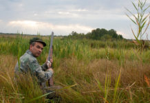 Restituire il tesserino venatorio: la situazione in Lombardia ed Emilia Romagna Restituire il tesserino venatorio Lombardia Emilia Romagna: cacciatore seduto nell'erba con fucile in mano