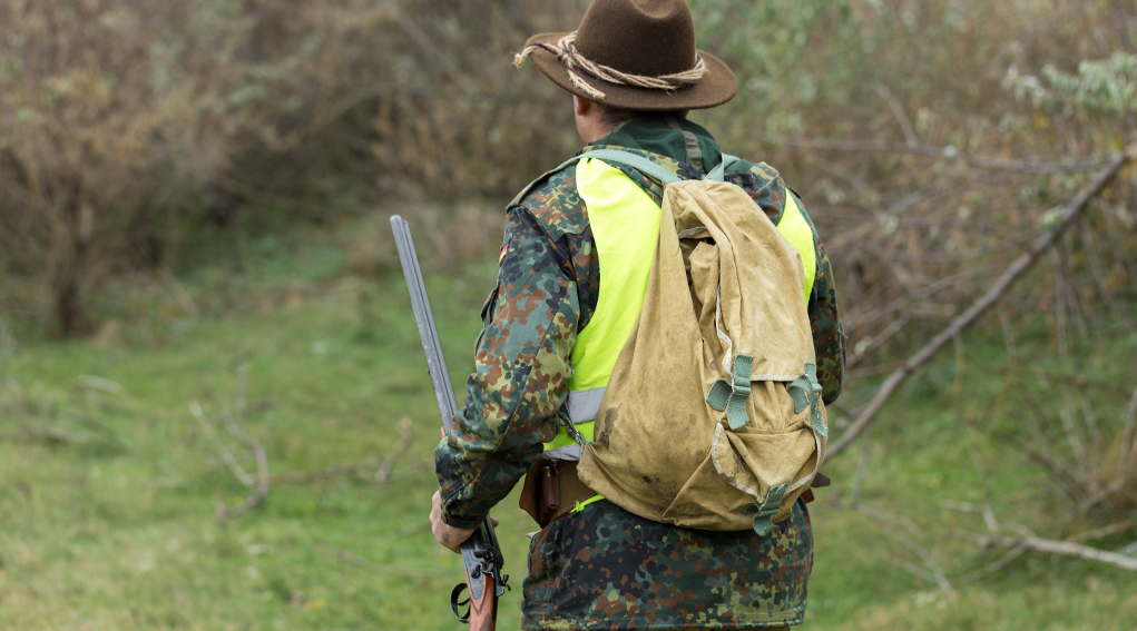 Iscrizione agli Atc toscani: cacciatore di spalle con cappello, zaino e gilet alta visibilità, fucile nella mano sinistra