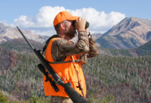 La caccia nella fase 2 dell’emergenza sanitaria: la cabina di regia chiede incontro al governo caccia nella fase 2 dell’emergenza sanitaria: cacciatore con gilet alta visibilità guarda nel binocolo, carabina a tracolla