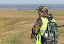 Proroga delle scadenze venatorie in Lombardia: ecco le date Proroga delle scadenze venatorie in Lombardia: cacciatore di spalle in alta visibilità, zaino sulle spalle, fucile in mano