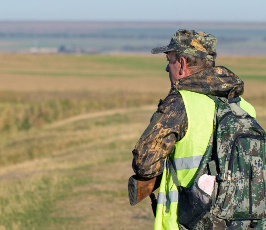 Proroga delle scadenze venatorie in Lombardia: ecco le date Proroga delle scadenze venatorie in Lombardia: cacciatore di spalle in alta visibilità, zaino sulle spalle, fucile in mano