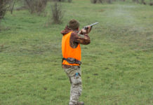Caccia in Lombardia, Regione valuta nuove proroghe Caccia in Lombardia: cacciatore di spalle con fucile imbracciato, gilet arancione alta visibilità