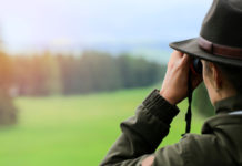 “Prima della stagione venatoria 2020/2021 tornate sui campi di tiro e in armeria” stagione venatoria 2020/2021: cacciatore in abbigliamento tradizionale guarda attraverso il binocolo