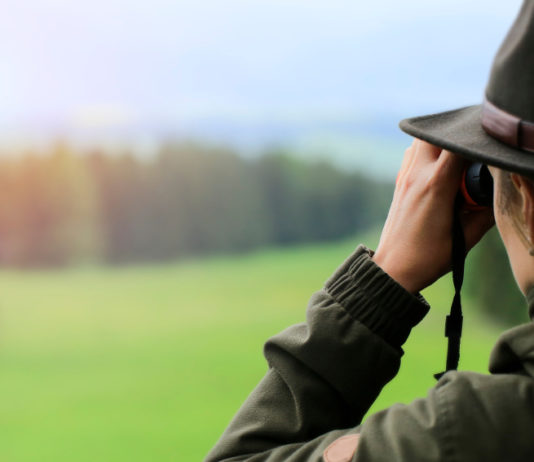 “Prima della stagione venatoria 2020/2021 tornate sui campi di tiro e in armeria” stagione venatoria 2020/2021: cacciatore in abbigliamento tradizionale guarda attraverso il binocolo