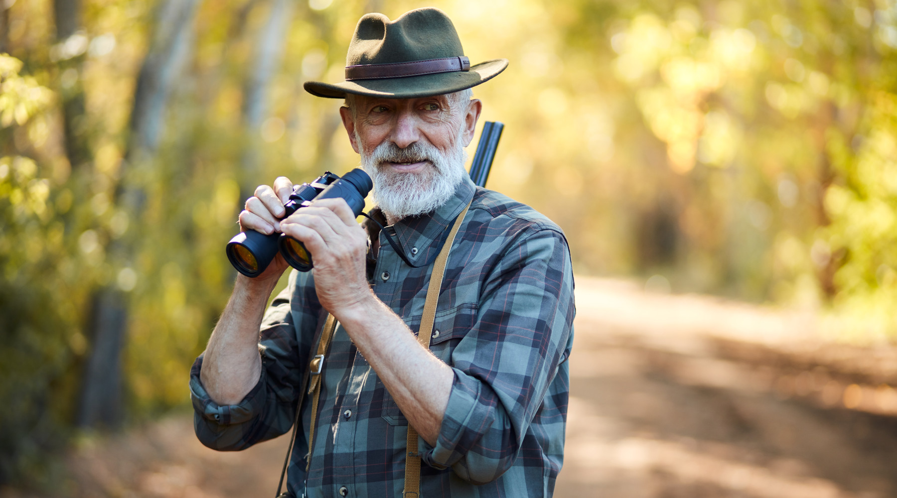 caccia e conservazione: cacciatore anziano con binocolo tra le mani e fucile in spalla