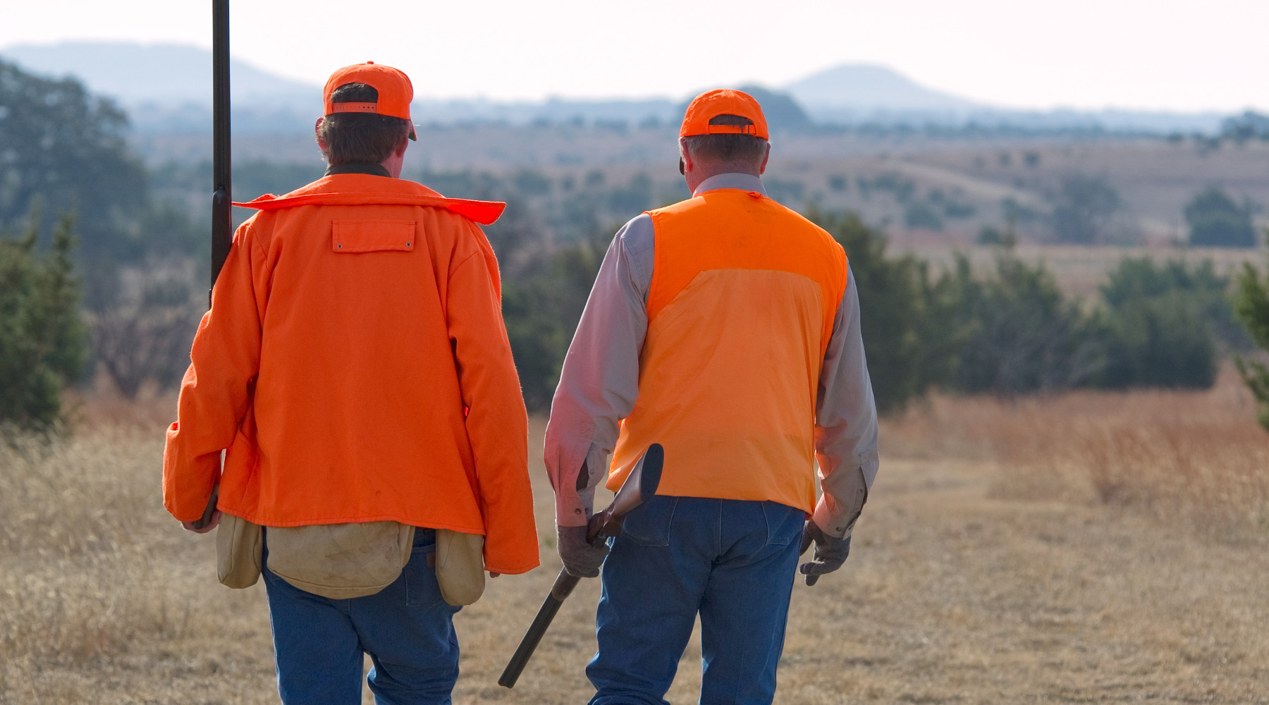 Associazione unica dei cacciatori: due cacciatori di spalle indossano gilet arancio alta visibilità