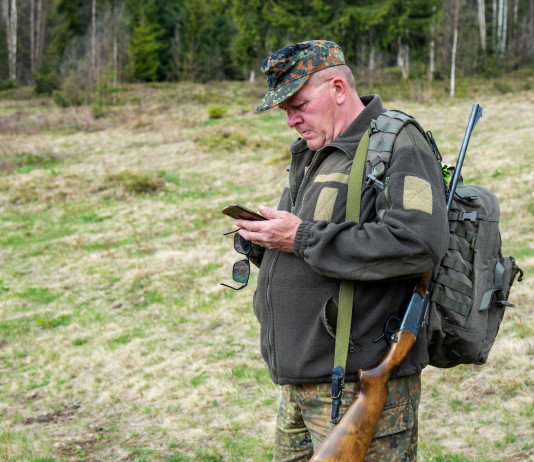 Agrivenatoria biodiversitalia, la posizione di Federcaccia Agrivenatoria biodiversitalia: cacciatore con zaino e fucile in spalla controlla telefono